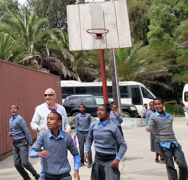 Jeff Hoffman walking with schoolchildren in uniform past a basketball hoop