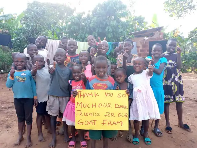 About eighteen children holding a hand-lettered sign thanking supporters for their goat farm
