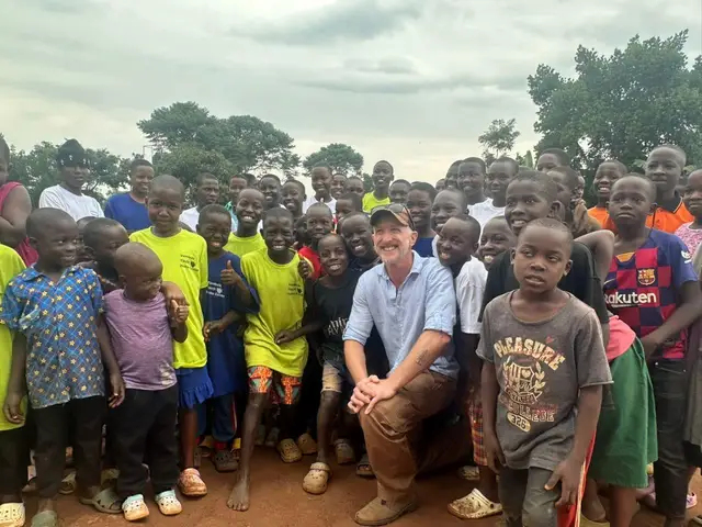 A donor kneeling among a large group of smiling children outside a youth home