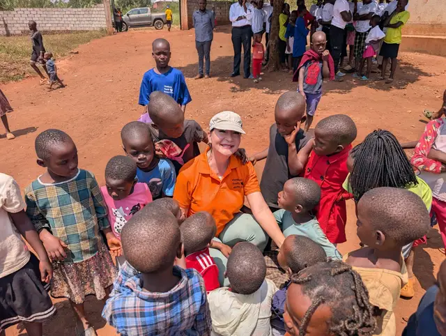 A woman in a Vumbula Youth Home Centre polo sitting among smiling children