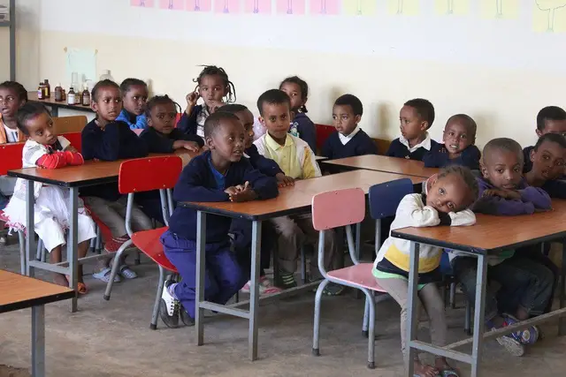 A classroom of young children in navy uniforms seated at wooden desks